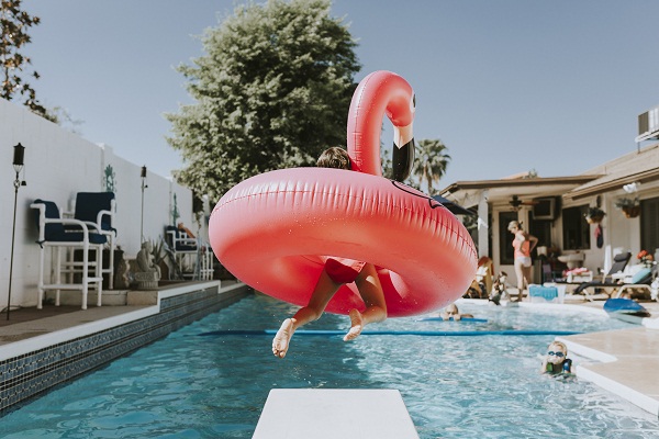 Girl jumping into swimming pool with pink flamingo