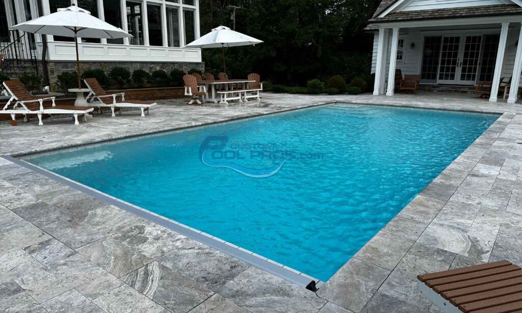 In-ground swimming pool with crystal clear blue water, surrounded by a stone patio, outdoor seating, and a shaded umbrella. Ideal for relaxation and outdoor gatherings, inground swimming pools