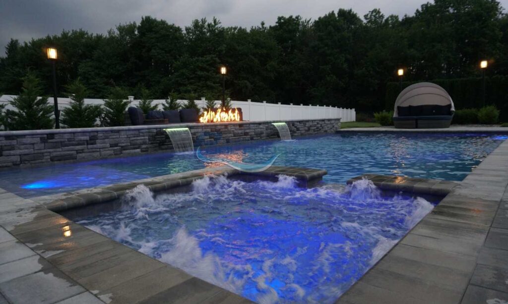 Luxury outdoor swimming pool with illuminated blue water, featuring cascading waterfalls and a serene landscaped background, ideal for relaxation and entertainment, inground pool