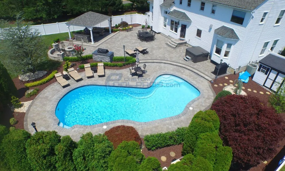 Aerial view of a beautiful backyard featuring a large swimming pool, surrounded by lounge chairs and landscaped gardens, with a gazebo and outdoor seating area in the background. Ideal for outdoor relaxation and entertainment. Inground pool contractors, swimming pool contractors nj