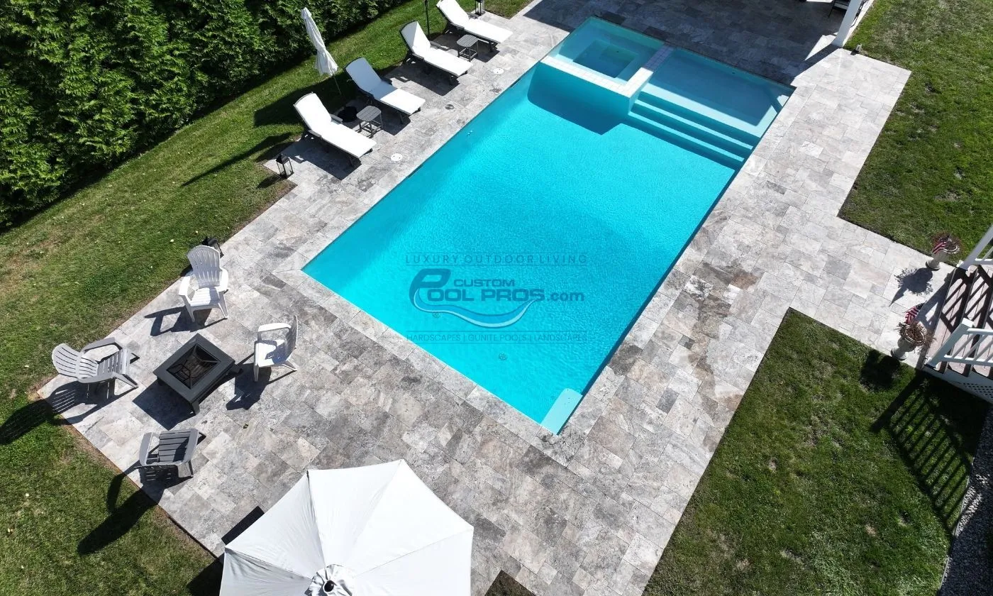 square shaped pool with spa and sun tanning ledge with stairs, pool deck with lounge chairs, firepit area, umbrella, pool builders