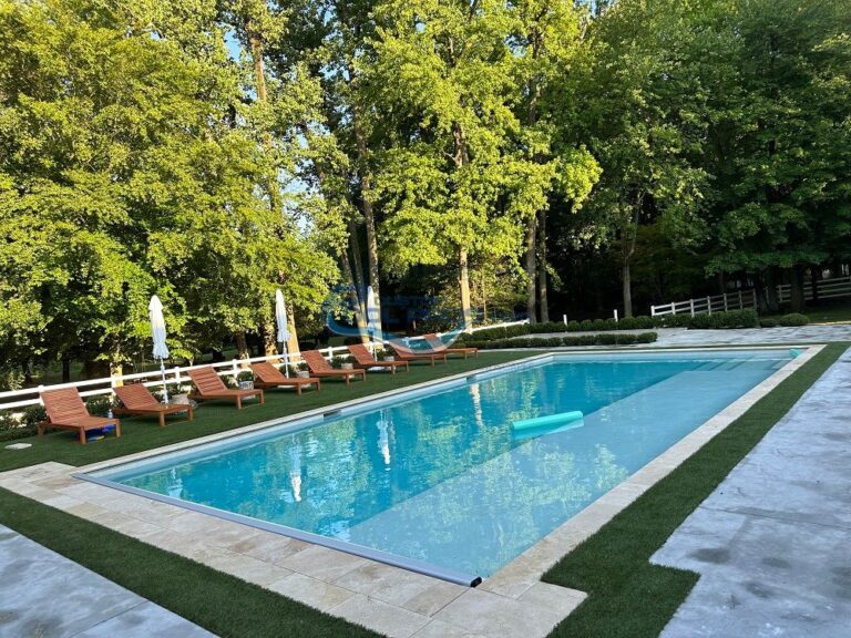 Outdoor swimming pool surrounded by lounge chairs and lush greenery, featuring a tranquil setting with sun umbrellas and well-maintained landscaping, pool installation new jersey