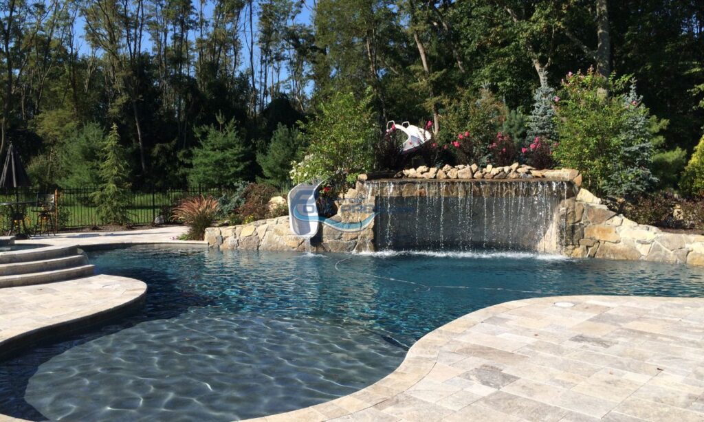 inground freeform pool with spa, grotto waterfall, slide, travertine pool deck patio installation, backyard pools