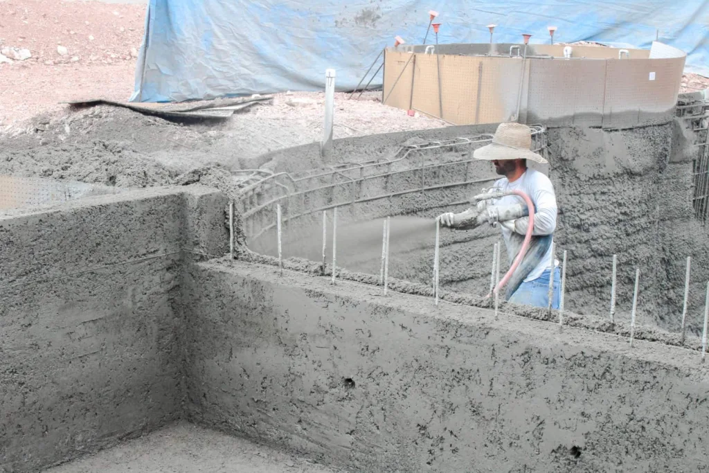 Man spraying gunite onto dug-out pool walls. 